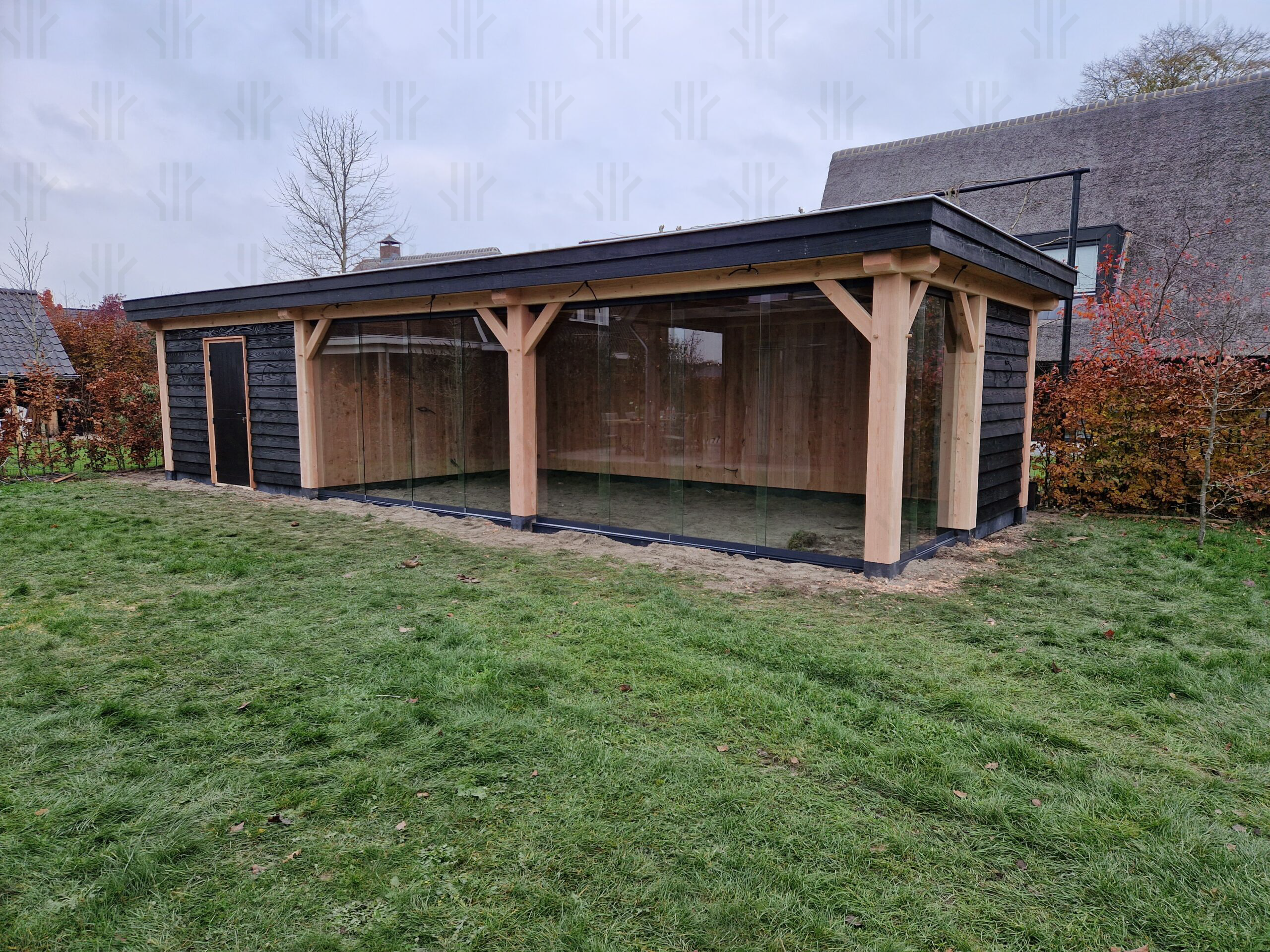 Overkapping maatwerkconstructie met glaswand uitgevoerd in een combinatie van zwart en blank Douglas hout